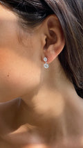 Close-up of a person wearing a silver earring with a clear gemstone.
