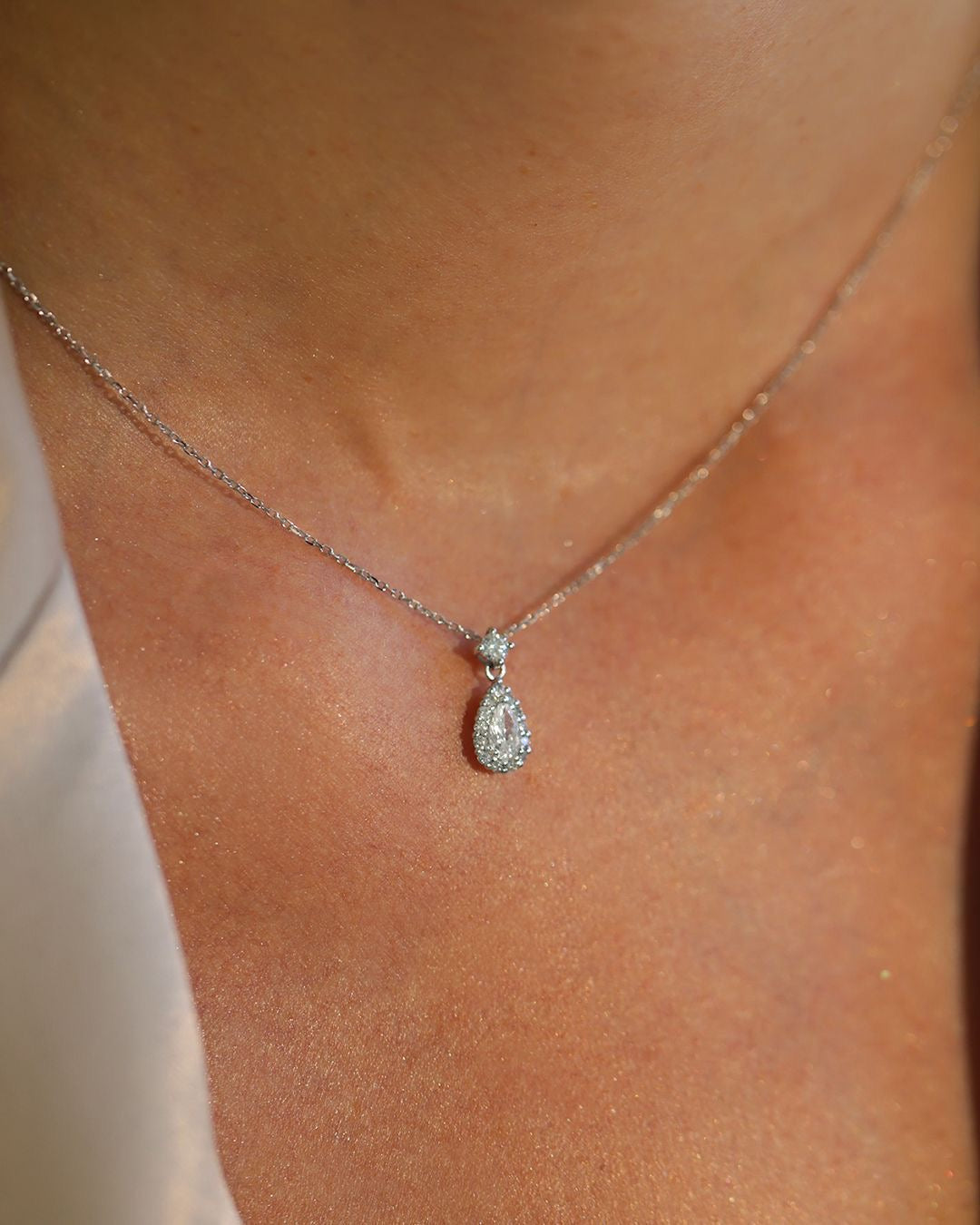 Teardrop-shaped diamond pendant on a necklace against a skin background