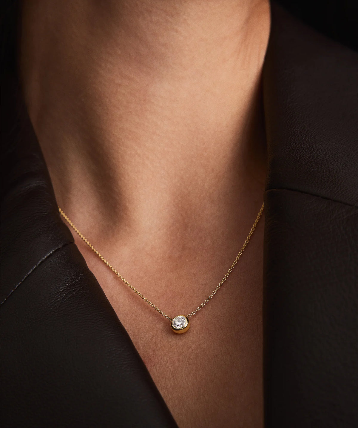 Gold necklace with a diamond pendant on a person's neck against a dark background