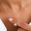 Woman's wearing a delicate gold chain necklace with a small starfish-shaped pendant adorned with tiny clear stones, resting near the chest.