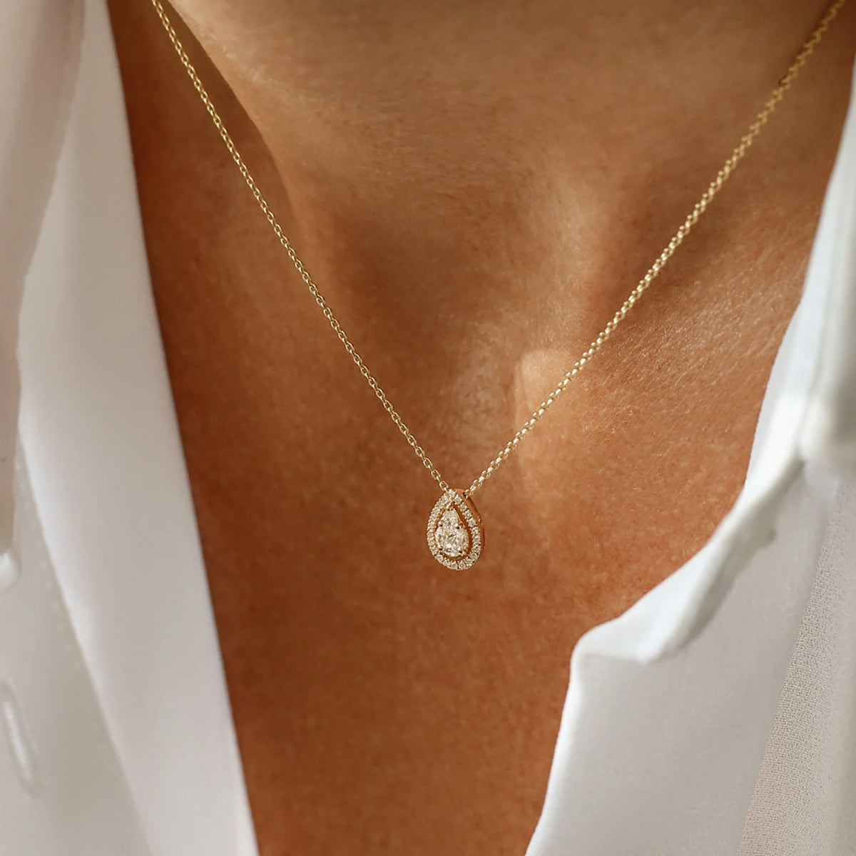 Gold necklace with a teardrop-shaped pendant on a person wearing a white top.