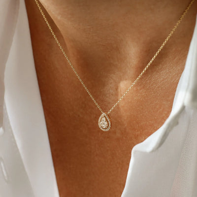 Gold necklace with a teardrop-shaped pendant on a person wearing a white top.